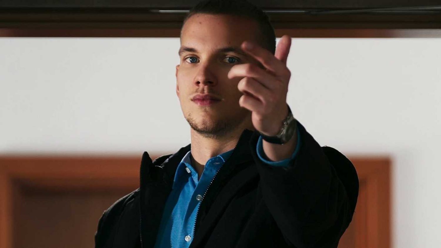 Ein junger Mann wingt uns herbei. Ernster Blick.